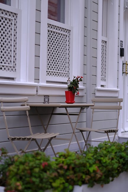 A small front garden in a residential terrace featuring a variety of lush, healthy plants and shrubs arranged along the pathway leading to a wooden front door. The garden beds are filled with colorful
